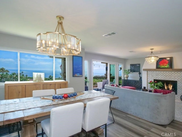 dining space with a tiled fireplace, a notable chandelier, wood finished floors, and visible vents