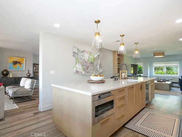 kitchen with sink, a kitchen island with sink, light brown cabinets, and light wood-type flooring