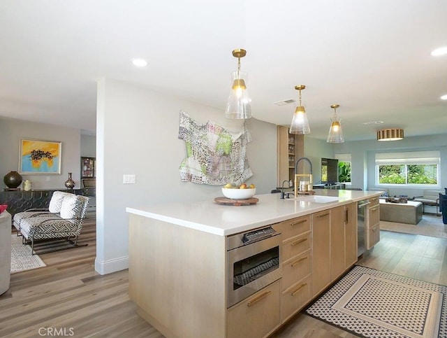 kitchen featuring light wood finished floors, open floor plan, light brown cabinetry, and a sink