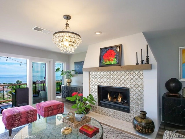 living room with a water view, a tiled fireplace, hardwood / wood-style floors, and a notable chandelier