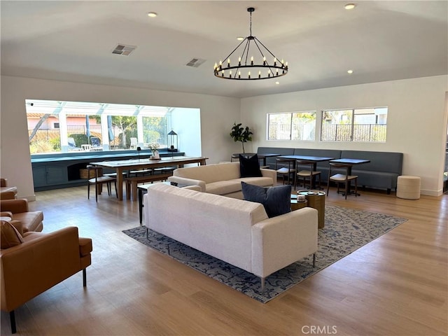 living area with visible vents, a healthy amount of sunlight, light wood-style flooring, and an inviting chandelier