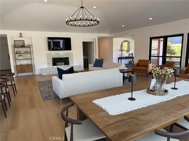 dining area featuring recessed lighting, an inviting chandelier, a high end fireplace, and light wood finished floors