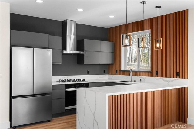 kitchen featuring gray cabinets, appliances with stainless steel finishes, pendant lighting, sink, and wall chimney exhaust hood