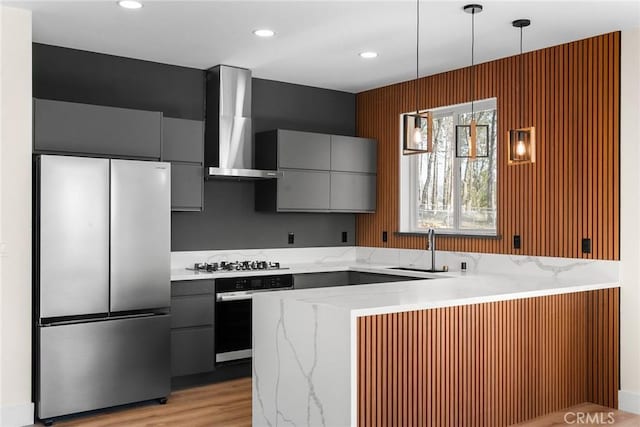 kitchen with sink, hanging light fixtures, appliances with stainless steel finishes, gray cabinets, and wall chimney range hood