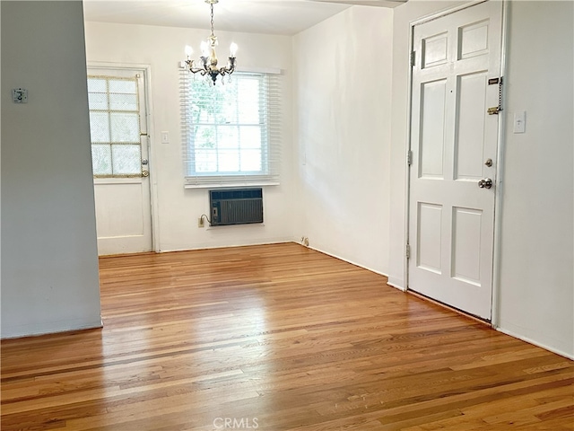 unfurnished dining area featuring hardwood / wood-style flooring, a healthy amount of sunlight, a wall mounted AC, and a notable chandelier