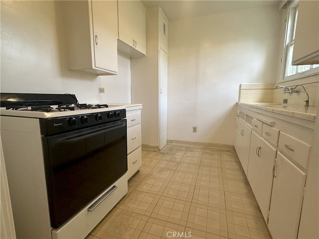 kitchen with sink, white cabinetry, range with gas stovetop, decorative backsplash, and tile countertops