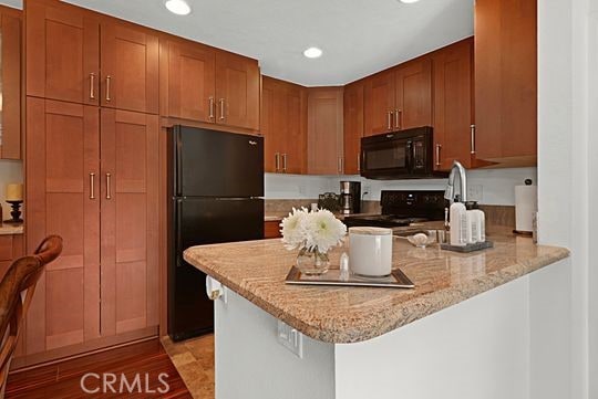 kitchen featuring light stone counters, light hardwood / wood-style floors, black appliances, a kitchen bar, and kitchen peninsula