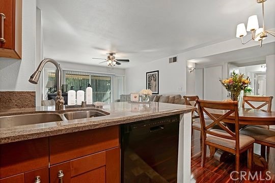 kitchen with sink, light stone counters, dark hardwood / wood-style floors, dishwasher, and ceiling fan with notable chandelier