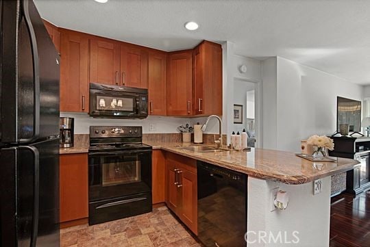 kitchen with a breakfast bar, sink, light stone counters, kitchen peninsula, and black appliances