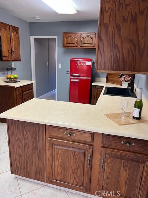 kitchen with light tile patterned floors, light countertops, a peninsula, and a sink