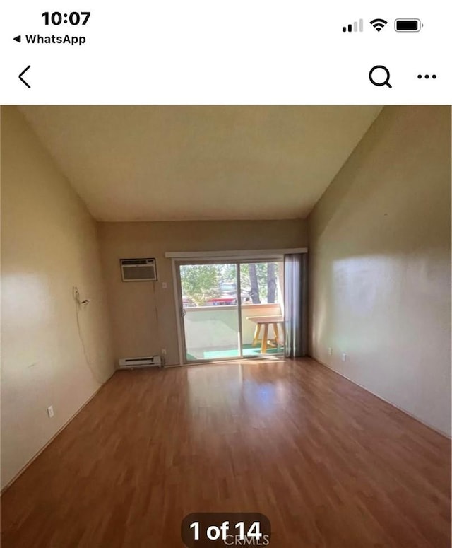 spare room featuring hardwood / wood-style flooring, lofted ceiling, a baseboard heating unit, and a wall mounted air conditioner