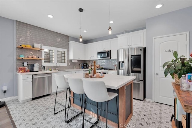 kitchen with sink, appliances with stainless steel finishes, white cabinetry, hanging light fixtures, and a center island