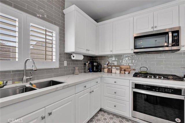 kitchen featuring appliances with stainless steel finishes, sink, white cabinets, backsplash, and light stone counters