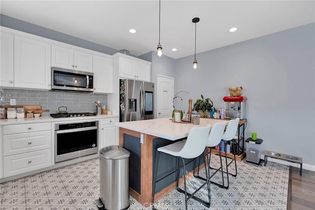 kitchen with white cabinetry, hanging light fixtures, appliances with stainless steel finishes, an island with sink, and decorative backsplash