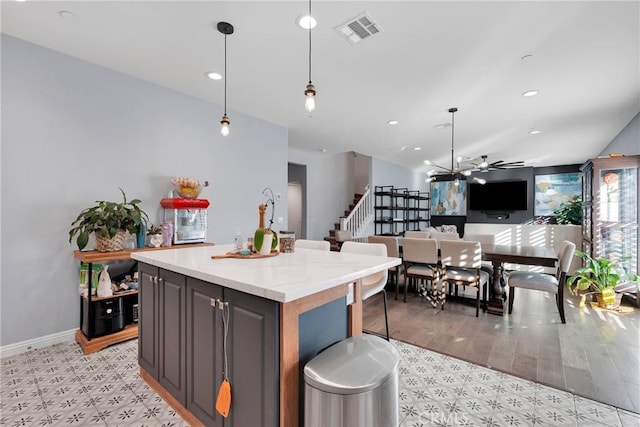 kitchen featuring a kitchen island, a breakfast bar, hanging light fixtures, ceiling fan, and light stone countertops