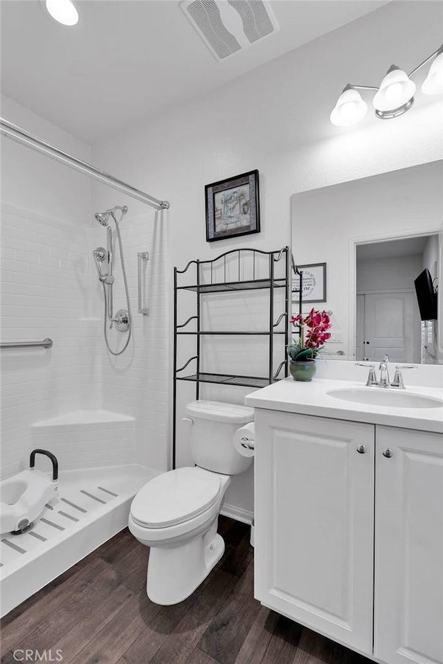 bathroom featuring hardwood / wood-style floors, vanity, a tile shower, and toilet