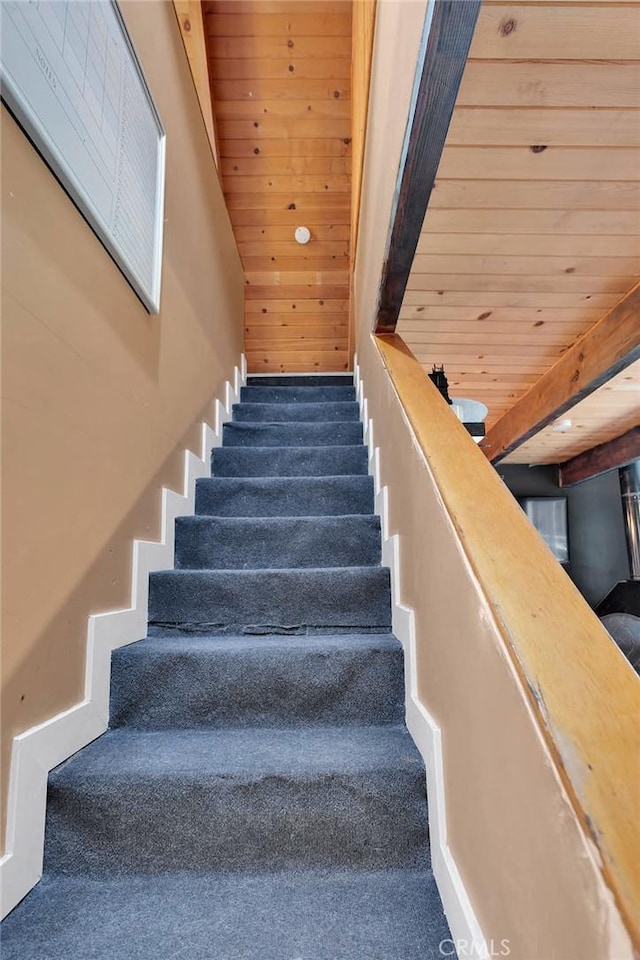 staircase featuring carpet flooring, wooden ceiling, and beam ceiling