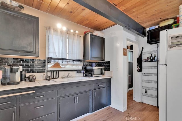 kitchen featuring sink, light wood-type flooring, wooden ceiling, white fridge, and decorative backsplash