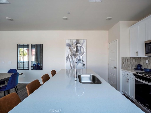 kitchen with sink, a breakfast bar area, white cabinetry, stainless steel appliances, and decorative backsplash