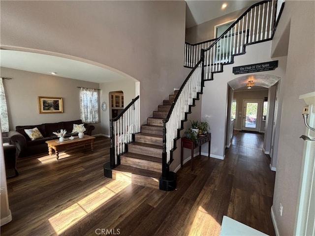 entrance foyer featuring stairway, arched walkways, baseboards, and wood finished floors