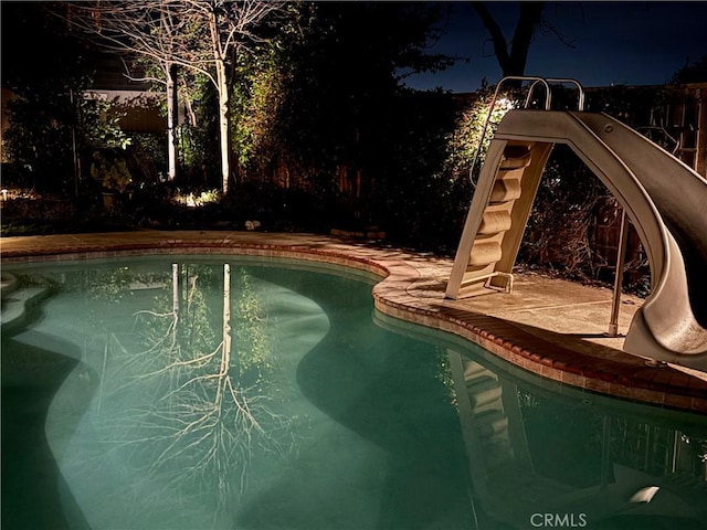 pool at twilight featuring a water slide and an outdoor pool