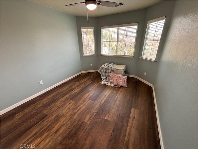 unfurnished room featuring baseboards, a ceiling fan, dark wood-style flooring, and a healthy amount of sunlight
