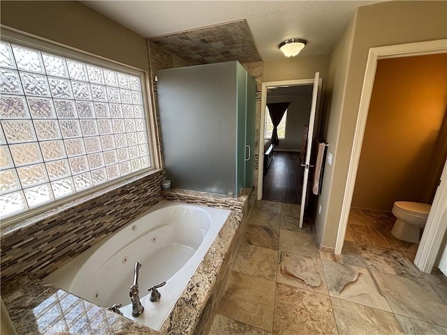 full bath with stone tile floors, toilet, and a tub with jets