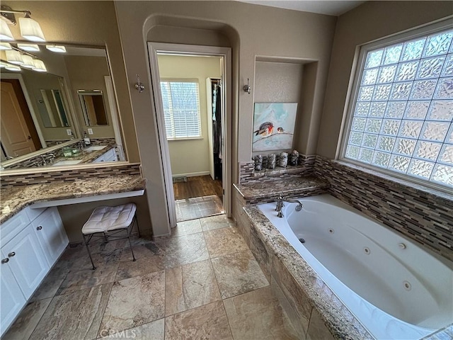 bathroom with stone tile floors, a whirlpool tub, a healthy amount of sunlight, and vanity