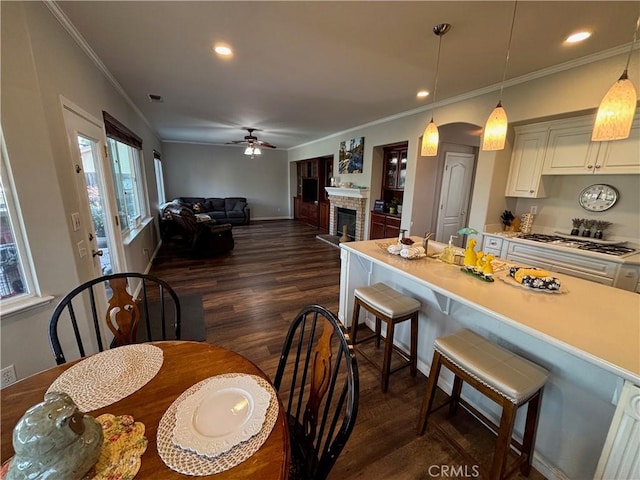 dining room featuring crown molding, ceiling fan, dark wood finished floors, and a fireplace