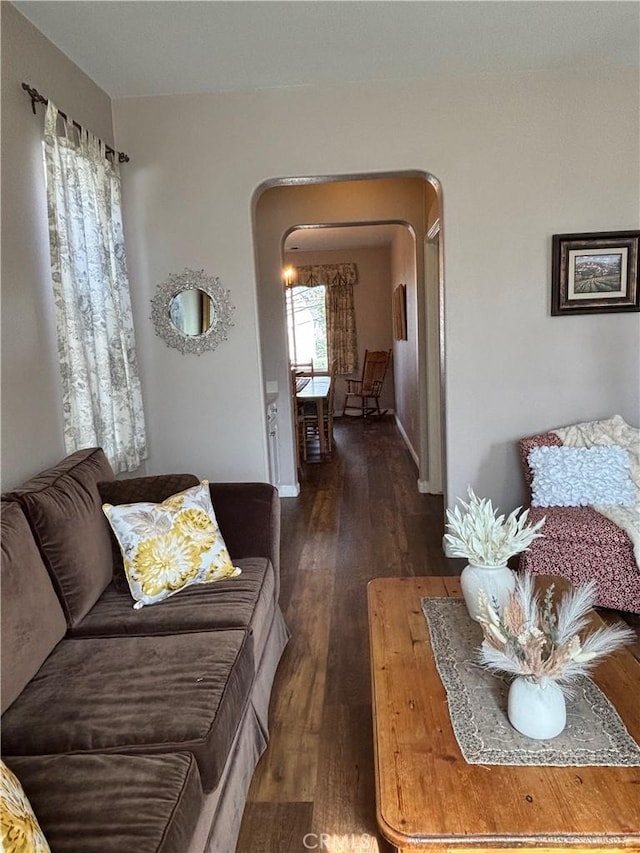 living area featuring baseboards, arched walkways, and dark wood-style floors