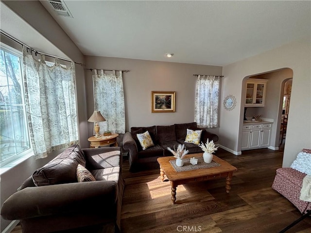 living area featuring baseboards, arched walkways, dark wood-style flooring, and visible vents