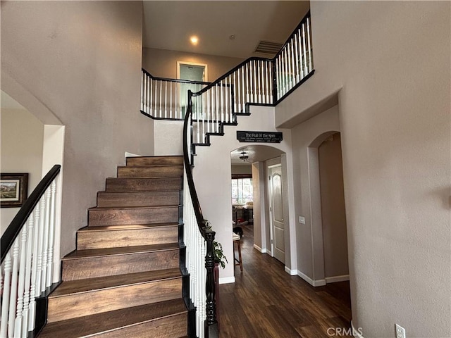 staircase featuring arched walkways, baseboards, wood finished floors, and a high ceiling