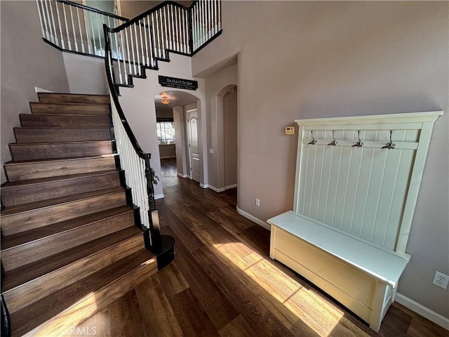 mudroom featuring arched walkways, baseboards, wood finished floors, and a high ceiling