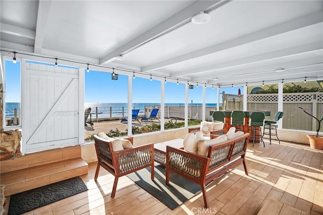 sunroom with beam ceiling, a barn door, and a water view