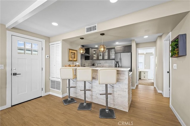 kitchen featuring light hardwood / wood-style flooring, stainless steel fridge with ice dispenser, a breakfast bar area, and kitchen peninsula