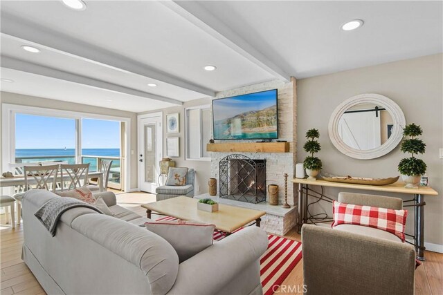 living room featuring a stone fireplace, beam ceiling, and light hardwood / wood-style flooring