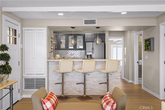 bar with hardwood / wood-style flooring, tasteful backsplash, hanging light fixtures, and stainless steel fridge