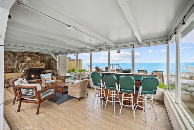 sunroom with beam ceiling, a wealth of natural light, a stone fireplace, and a water view