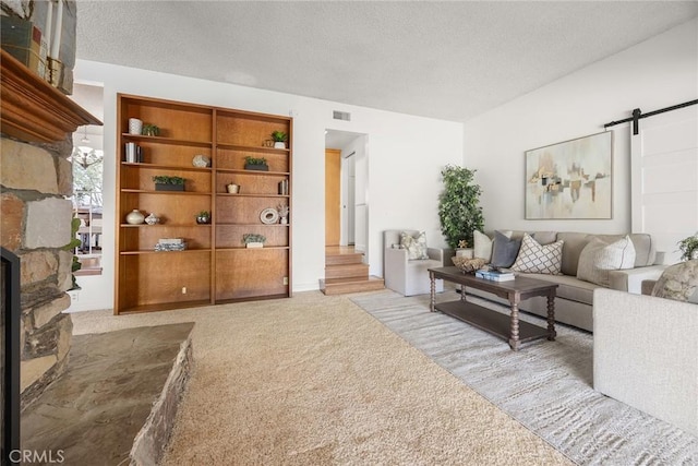 carpeted living room featuring a barn door, a fireplace, visible vents, and a textured ceiling