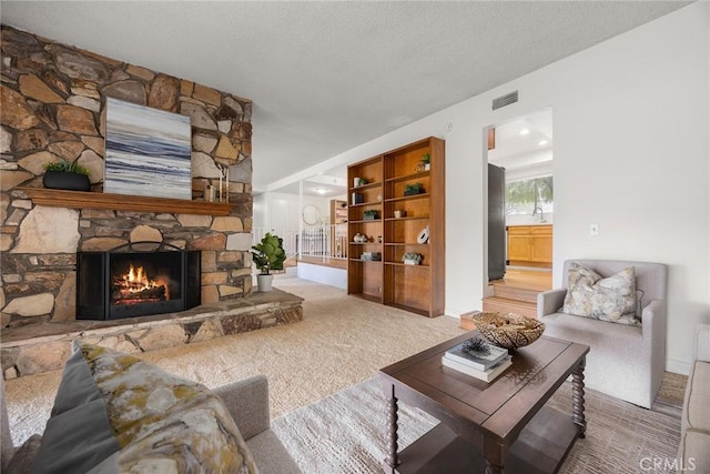 carpeted living room with sink, a stone fireplace, and a textured ceiling