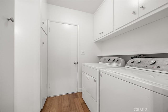 clothes washing area featuring cabinets, washing machine and dryer, and light wood-type flooring