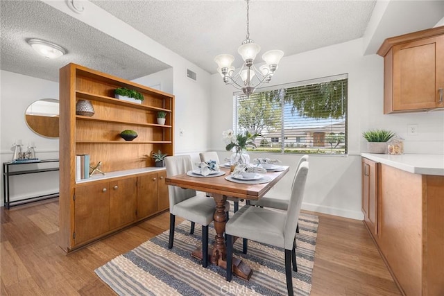 dining area with a notable chandelier, a textured ceiling, and light wood-type flooring