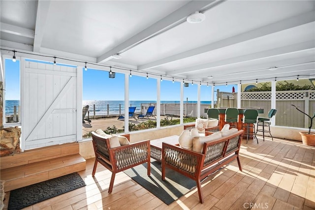 sunroom featuring a barn door, a water view, and beam ceiling