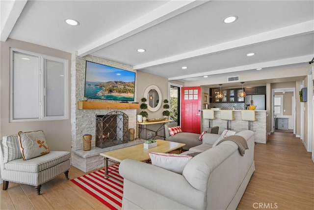 living room featuring beamed ceiling, a fireplace, and light hardwood / wood-style floors