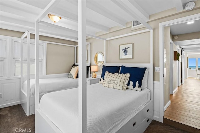 bedroom with a barn door, beam ceiling, and dark hardwood / wood-style flooring