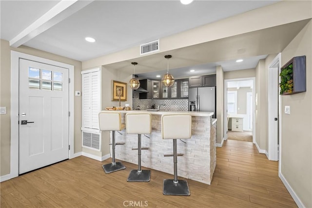 kitchen featuring light hardwood / wood-style floors, kitchen peninsula, a kitchen breakfast bar, and stainless steel fridge with ice dispenser