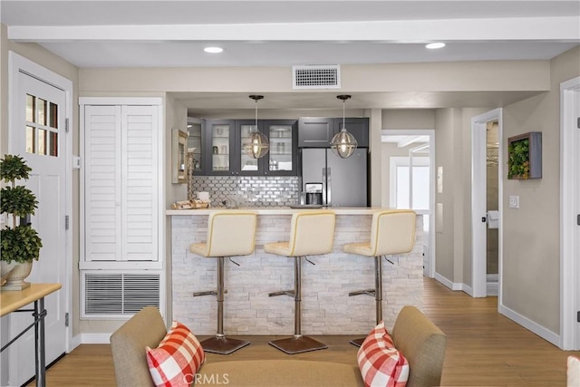 bar featuring pendant lighting, stainless steel fridge with ice dispenser, hardwood / wood-style flooring, and decorative backsplash