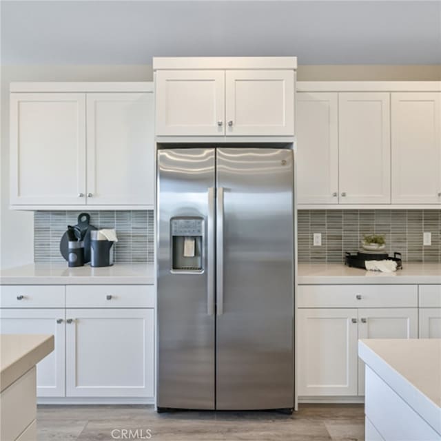 kitchen featuring white cabinetry, stainless steel fridge with ice dispenser, light hardwood / wood-style flooring, and backsplash