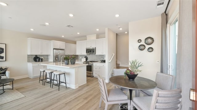 kitchen with white cabinetry, appliances with stainless steel finishes, a kitchen island with sink, and a breakfast bar area