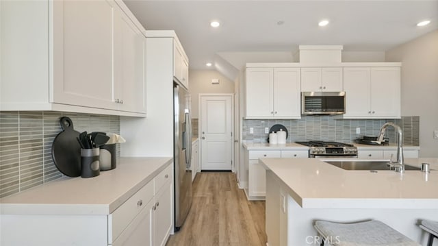 kitchen with sink, light hardwood / wood-style flooring, stainless steel appliances, tasteful backsplash, and white cabinets